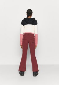 Bluza z kapturem w kolorowe bloki w czerni, kremie i różu. Połączona z bordowymi spodniami z zamkami błyskawicznymi i rozszerzanym krojem.