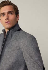 Chaqueta de espiga gris con cuello alto, acentos en negro contrastantes y tejido texturizado. Presenta bolsillos frontales y detalles de corte ajustado.