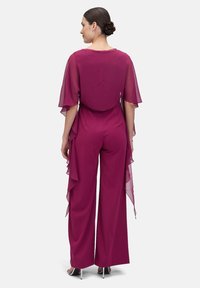 Mauve jumpsuit with short flutter sleeves, flowy side drapes, and wide-leg design. Smooth fabric with subtle sheen and back detail.