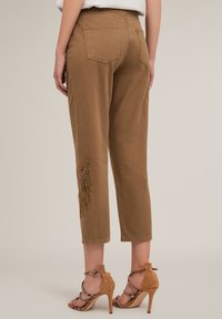 Bruine cropped pants met een gladde textuur en geborduurde bloemenmotieven op het onderbeen, gecombineerd met tan geklede sandalen met hoge hakken.