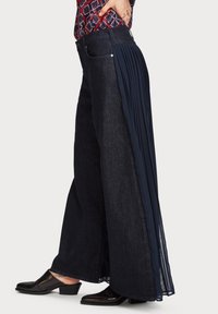 Pantalon en denim à jambes larges avec un délavage foncé, doté d'un panneau en tissu navy plissé s'étendant à partir de la couture latérale pour une texture et un design ajoutés.