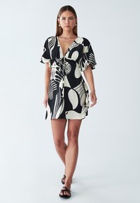 Schwarz-weiß bedrucktes Kleid mit kurzen Ärmeln, tiefem Ausschnitt und tailliertem Bund. Es zeichnet sich durch abstrakte Muster und eine lockere, fließende Passform aus.