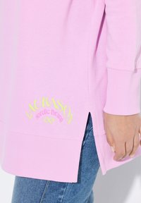 Sudadera rosa claro de gran tamaño con puños acanalados y aberturas laterales, que presenta un logo bordado en amarillo que dice "LAURASON Nordic Brand."