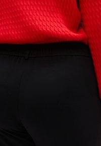 Κόκκινο υφαντό πουλόβερ συνδυασμένο με μαύρο ελαστικό παντελόνι, που αναδεικνύει έναν ομαλό, εφαρμοστό σχεδιασμό στη μέση. Χωρίς ορατά μεταλλικά στοιχεία ή σχέδια.