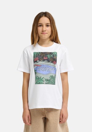 Jeune personne portant un t-shirt blanc avec un graphisme coloré d'une piscine entourée de plantes et d'arbres.