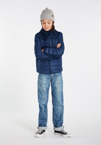 Mørkeblå pufferjakke med hætte, lynlås foran og brystlomme. Matcher med lyseblå jeans og sorte sneakers. Grå strikket hue på hovedet.