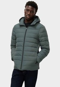 Gewatteerd jack in gedempt groen met horizontale steken, een ritssluiting aan de voorkant en een capuchon. De stof oogt glad met een licht glanzende afwerking.