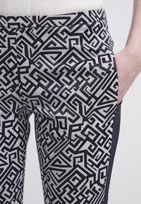 Svart och vitt mönstrat tyg med intrikata geometriska mönster på byxor med sidoficka. Slät textur, åtsittande form.