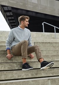 Black high-top sneakers with gray accents, textured fabric upper, white sole, paired with beige chinos and a light gray sweater.