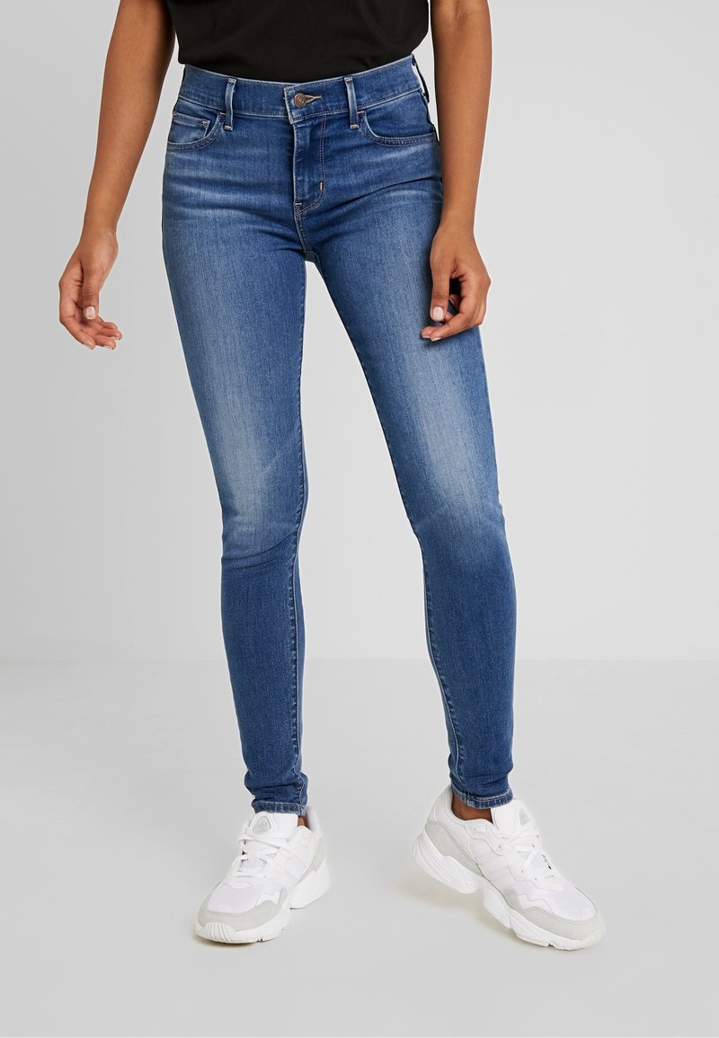 Smala blå jeans i denim med en slät yta, med hög midja, ljus blekning på låren och standard femficksdesign.