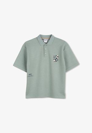 Polo vert en tissu texturé, avec une patte de boutonnage à trois boutons, une poche avec un logo, et un texte imprimé sur le côté inférieur.