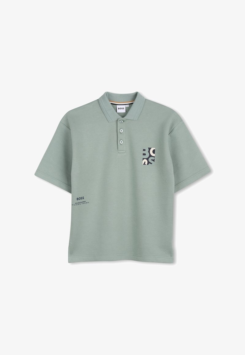 Polo vert en tissu texturé, avec une patte de boutonnage à trois boutons, une poche avec un logo, et un texte imprimé sur le côté inférieur.