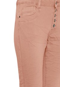 Gros plan d'un pantalon couleur pêche montrant les poches avant, les coutures et une rangée de boutons métalliques le long de la braguette.