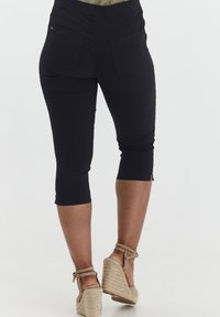 Pantalones cortos negros de corte ajustado, con una cintura sin costuras, dos bolsillos traseros, dobladillos enrollados y una textura de tela suave.
