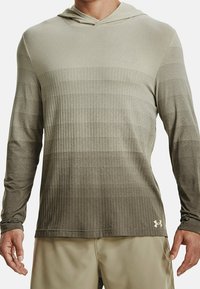 Maglietta a maniche lunghe con cappuccio di colore verde oliva chiaro, con un motivo a griglia testurizzato. Realizzata in tessuto leggero, presenta il logo Under Armour sull'orlo.