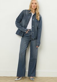 Veste en denim et jeans évasés en bleu foncé avec des accents métalliques. Comprend des boutons, des poches, et un design à jambes droites. Des chaussures argentées viennent compléter le look.
