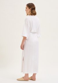 Abito bianco fino al ginocchio con maniche corte e spacchi laterali. Tessuto morbido con vestibilità comoda, accompagnato da scarpe slip-on beige chiaro.
