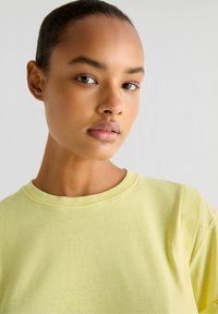 T-shirt in cotone giallo chiaro con scollatura tonda e maniche corte; presenta una texture morbida e liscia e dettagli di cucitura visibili.