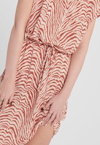 Vestido de manga corta, hasta la rodilla, en una tela texturizada de color crema con rayas de cebra en tono óxido; cuenta con una cintura ajustable y una abertura lateral.