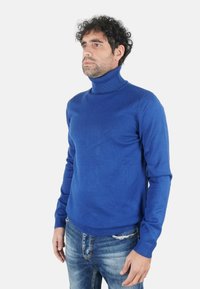 Maglione a collo alto blu in tessuto lavorato a maglia. Design aderente con scollo e polsini a costine. Abbinato a jeans denim usurati.