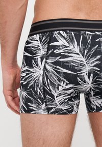 Boxer shorts neri con un motivo a foglia di palma bianca, caratterizzati da una cintura a strisce in contrasto e un design aderente.