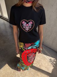 Μαύρο μπλουζάκι με ροζ γραφικό καρδιάς από λουλούδια, συνδυασμένο με πολύχρωμη φούστα με σχέδιο που περιλαμβάνει κόκκινες, μπλε και πράσινες λεπτομέρειες.