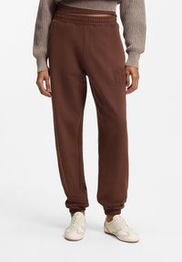 Brune joggingbukser med elastisk talje og manchetter, med et tonalt broderet logodetalje på låret. Glat tekstur, afslappet pasform.