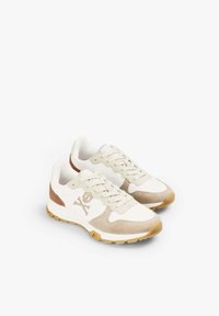 White sneaker with beige suede accents and tan rubber sole. Features a skull logo on the side and a textured lace area.