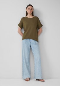 Olive green oversized t-shirt z krótkimi rękawami, w połączeniu z jasnoniebieskimi spodniami typu wide-leg. Prosty design z luźnym krojem. Sandały dopełniają całość.
