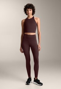 Bordo športni modrček in visoko pasne legice iz elastičnega materiala, v kombinaciji s črnimi športnimi čevlji. Gladka tekstura, prilega se telesu.