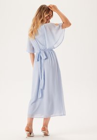 Ljusblå, svävande klänning med korta, genomskinliga ärmar, midjeband och lång kjol. Slät textur, längd till mitten av vaderna och öppen ryggdetalj.