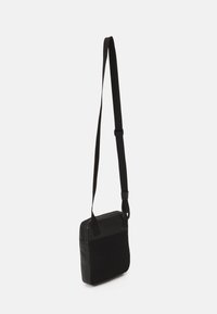 Borsa a tracolla nera con superficie testurizzata, finitura liscia, forma rettangolare, tracolla regolabile e chiusura a zip nella parte superiore.