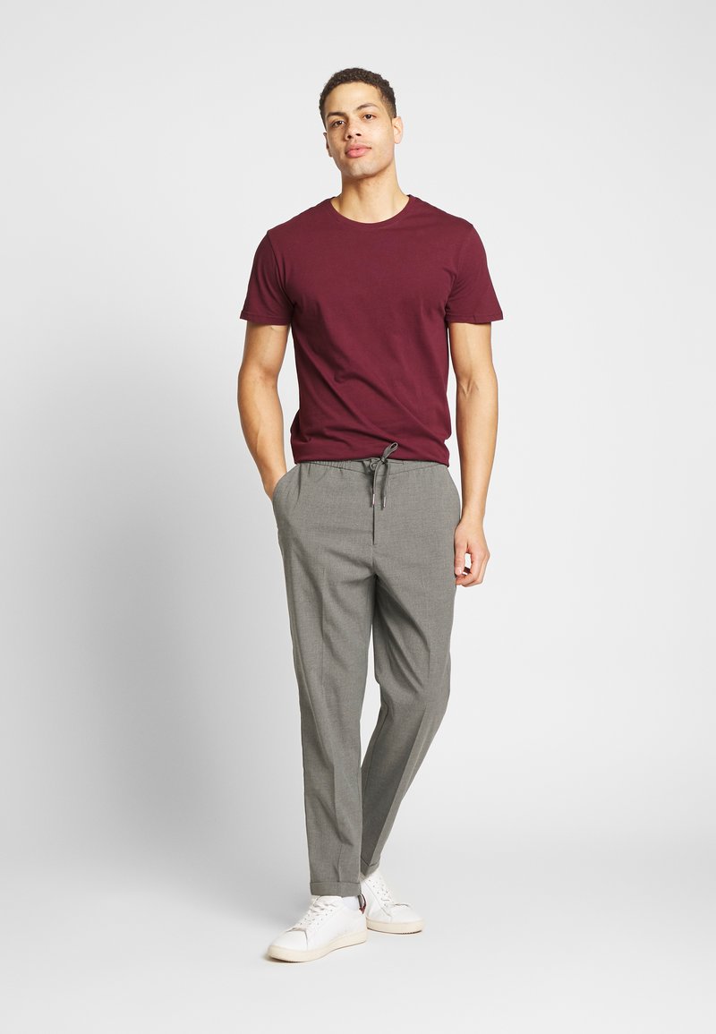 Camiseta burdeos combinada con pantalones claros de tejido gris. Los pantalones tienen una cintura con cordón y son ajustados en los puños. Zapatillas blancas completan el look.
