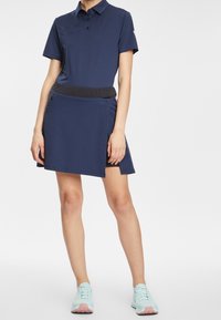 Mörkblå pikétröja med ribbad krage och tre knappar, ihopparad med en matchande kjol som har ett svart midjeband och sidoficka med dragkedja.