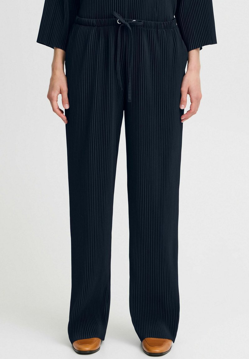 Pantalons noirs à jambes larges en tissu à ribbing texturé, dotés d'une taille élastique avec cordon de serrage et de jambes légèrement évasées.