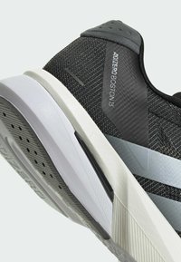 Zwarte gestructureerde hardloopschoen met grijze accenten, voorzien van een lichtgewicht ontwerp, gevoerde kraag en een patroonrubberen zool voor grip.