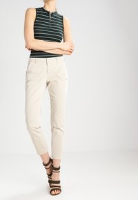 Grön och vit randig ärmlös topp med dragkedja i nacken. Beiga slim-fit byxor och bruna sandaler med klack och remmar.