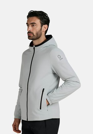 Giacca con cappuccio grigio chiaro con accenti neri, polsini elastici e tasche con zip, caratterizzata da un logo sulla spalla sinistra. Texture del tessuto liscia.