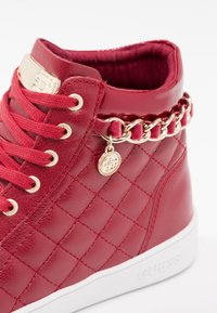 Red synthetic high-top sneaker with quilted texture, gold chain accent, logo plaque, and white rubber sole. Laced with matching red shoelaces.