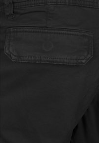 Pantalones de tela negra con un bolsillo trasero que tiene una solapa rectangular y detalles cosidos. El material tiene una textura suave y mate.