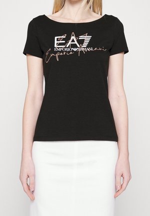 Žena nosící černé tričko s krátkým rukávem s logem "EA7 Emporio Armani" v bílé a růžově zlaté barvě, doplněné o bílou sukni.