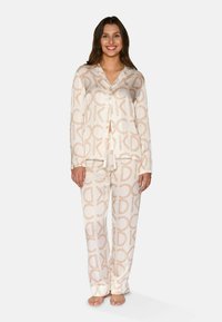Pyjama, jotka on valmistettu pehmeästä kankaasta, beige ja vaaleanruskea logo-kuvio. Setti sisältää napillisen paidan ja siihen sopivat housut.