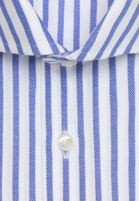 Camicia bianca con sottili strisce blu. Presenta un colletto classico, chiusura frontale con bottoni e un bottone standard di forma rotonda.