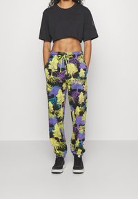 Person wearing a black cropped T-shirt and colorful joggers with neon tree and root patterns, paired with black sneakers.