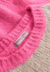 Roze en beige gebreide trui met geribbelde kraag; het label zegt "FRIEDA & FREDDI." De textuur lijkt fluffy, met een contrasterende kleursplit.