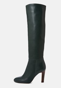 Botte femme en cuir vert foncé, hauteur genou, avec un bout pointu et un haut talon en bois, présentée de côté sur un fond blanc.