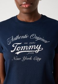 Mørkeblå bomulls t-skjorte med hvit slitt tekst: "Authentic Original Tommy Jeans New York City" og rund hals.