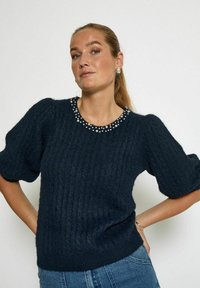 Navy cable-knit sweater with short puff sleeves, adorned with a beaded neckline. Soft texture and relaxed fit. Paired with denim.