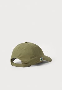 Olivengrønn caps med buet skjerm, laget av teksturert stoff, med en liten brodert logo på siden og en justerbar stropp bak.
