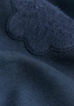 Navyblauer Stoff mit glatter Textur, versehen mit einem flauschigen marineblauen Patch mit gewelltem Rand, der auf das Material genäht ist.